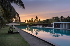 A serene pool area with lounge chairs and a palm tree, surrounded by lush greenery and a clear sky.