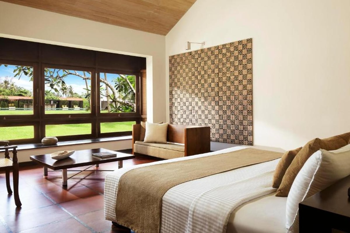 A bedroom with a large window, a bed, a bedside table, and a patterned wall.