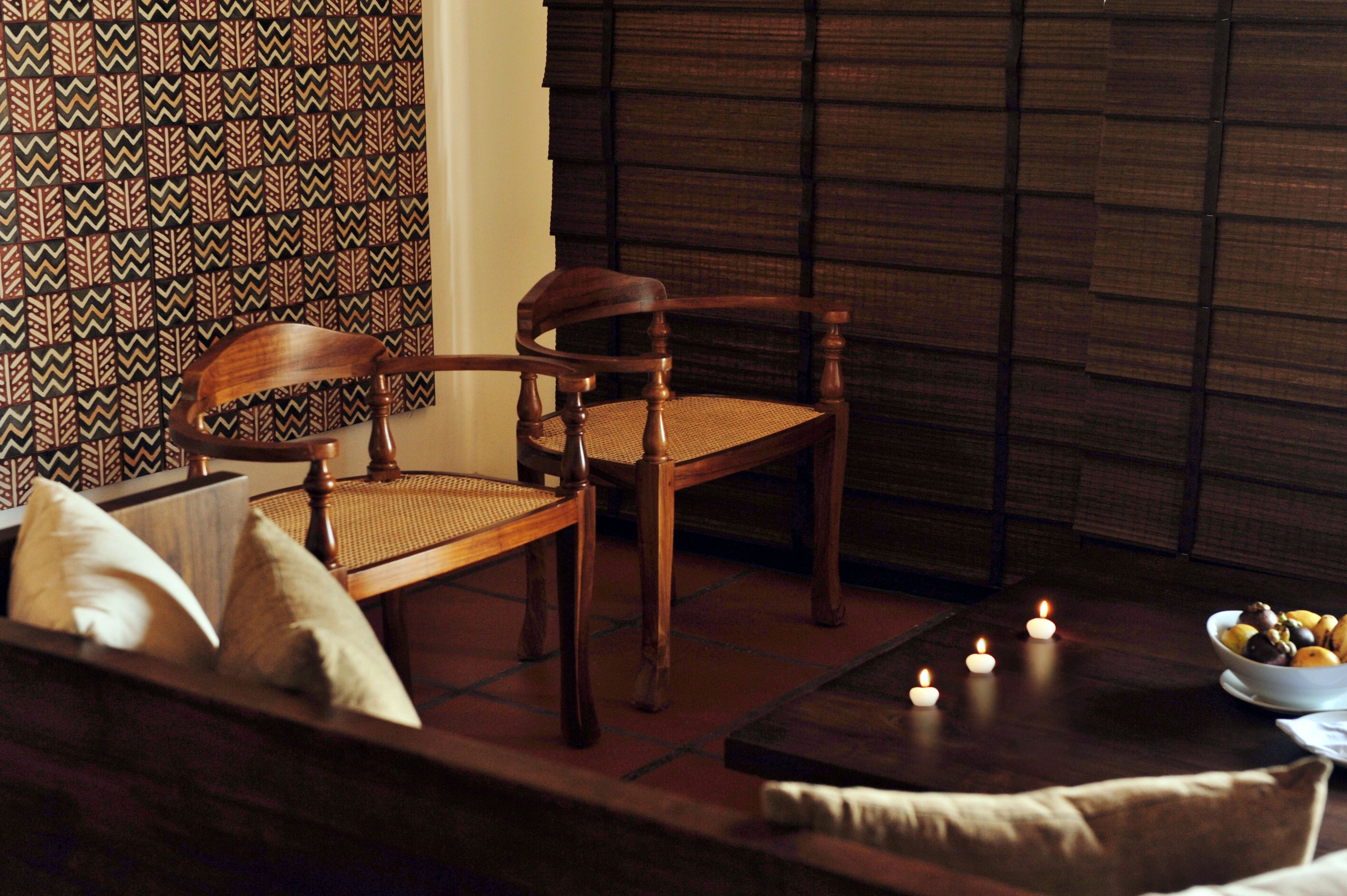 A cozy seating area with a wooden chair and sofa, a small table with candles, and a patterned wall.