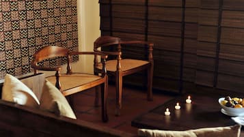 Un coin salon accueillant avec une chaise et un canapé en bois, une petite table avec des bougies et un mur orné de motifs.