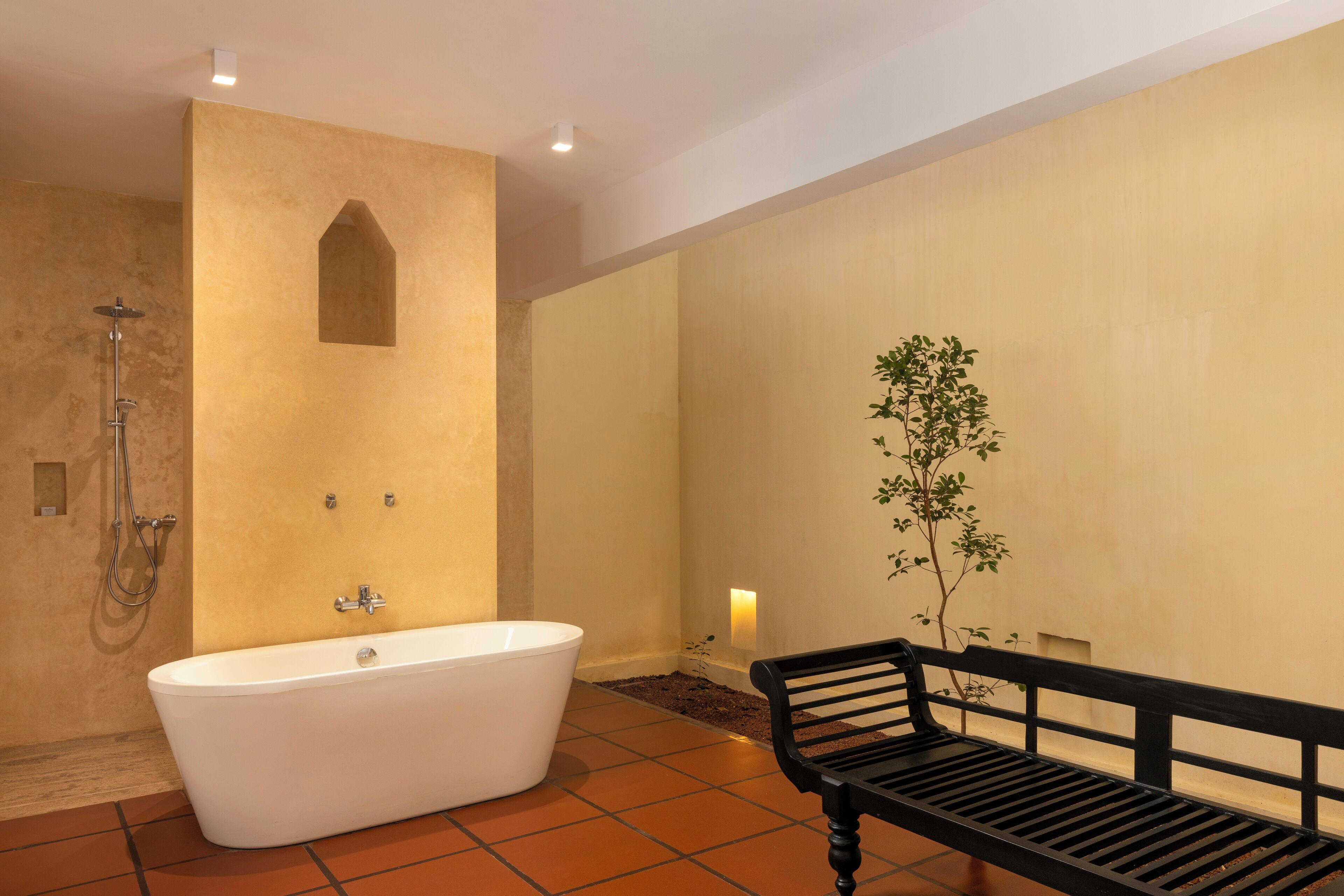 Un baño con una bañera independiente, un banco y una planta pequeña.