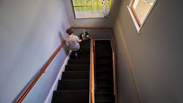 A person descending a staircase with a handrail, a window with a view of a wooden deck, and a wall-mounted artwork.