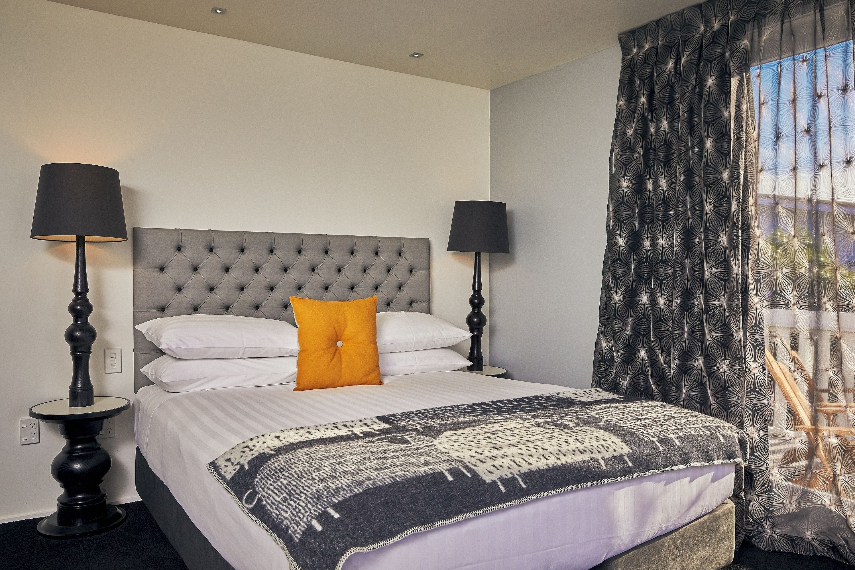 A neatly made bed with a patterned throw, two bedside lamps, and a tufted headboard.