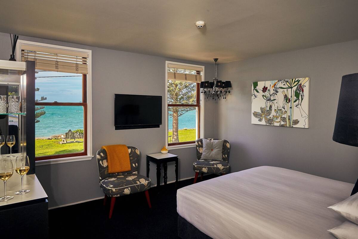 Habitación de hotel con cama, dos sillas, una mesita, televisor y ventana con vista al mar.