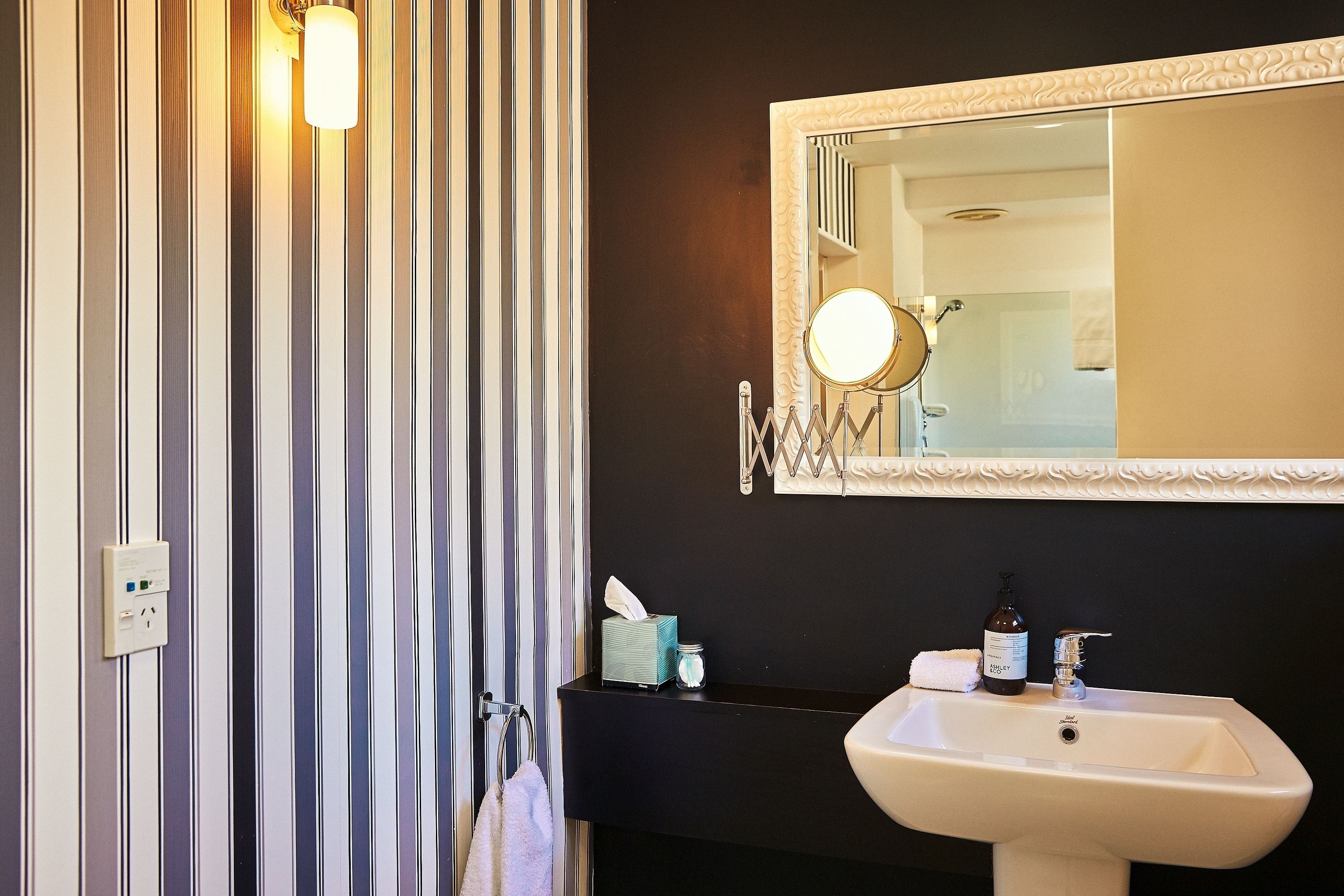 Un baño con cortina de ducha a rayas, un lavabo con espejo arriba y artículos de aseo en la encimera.