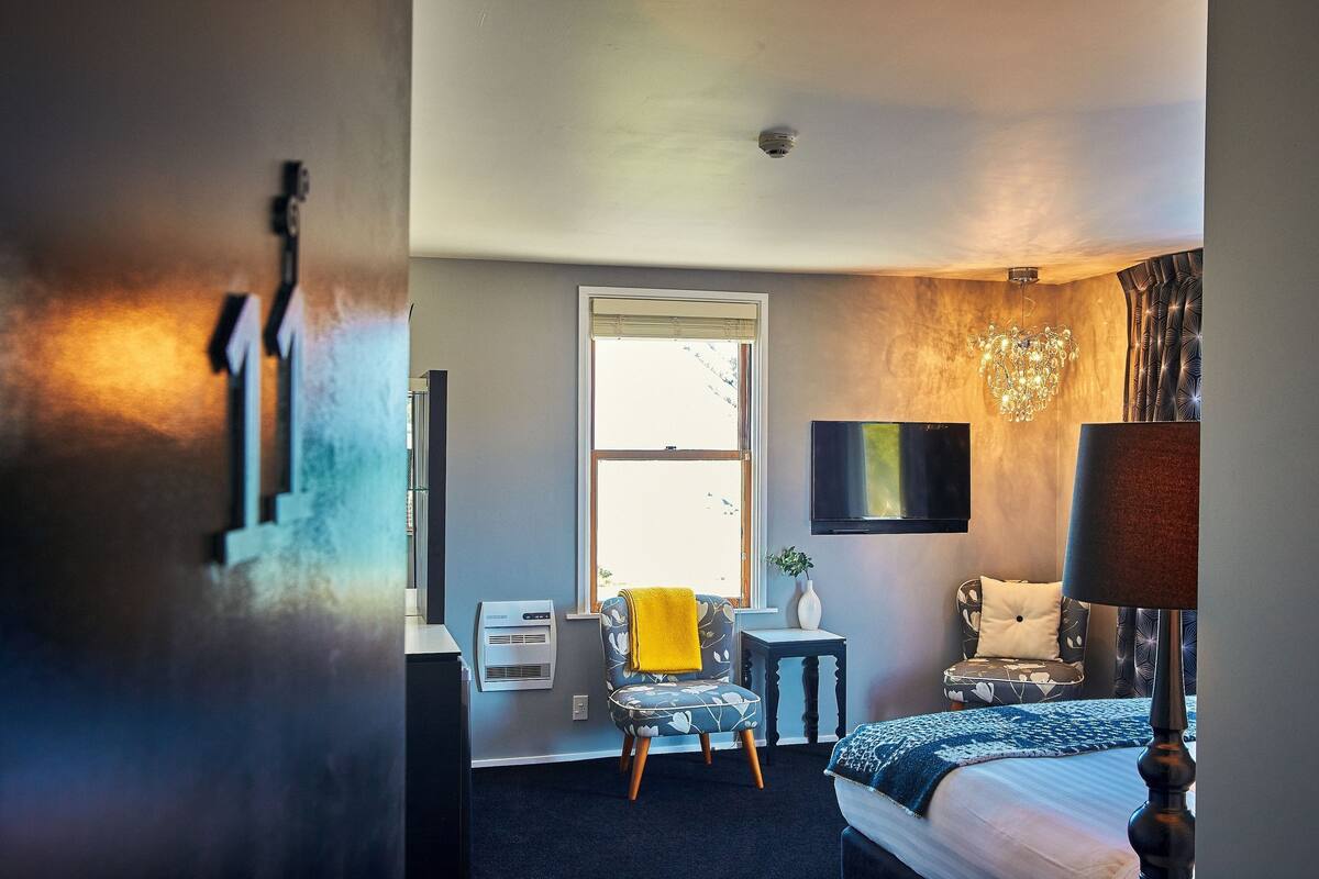 Una habitación de hotel con cama, escritorio, silla, televisor y ventana.