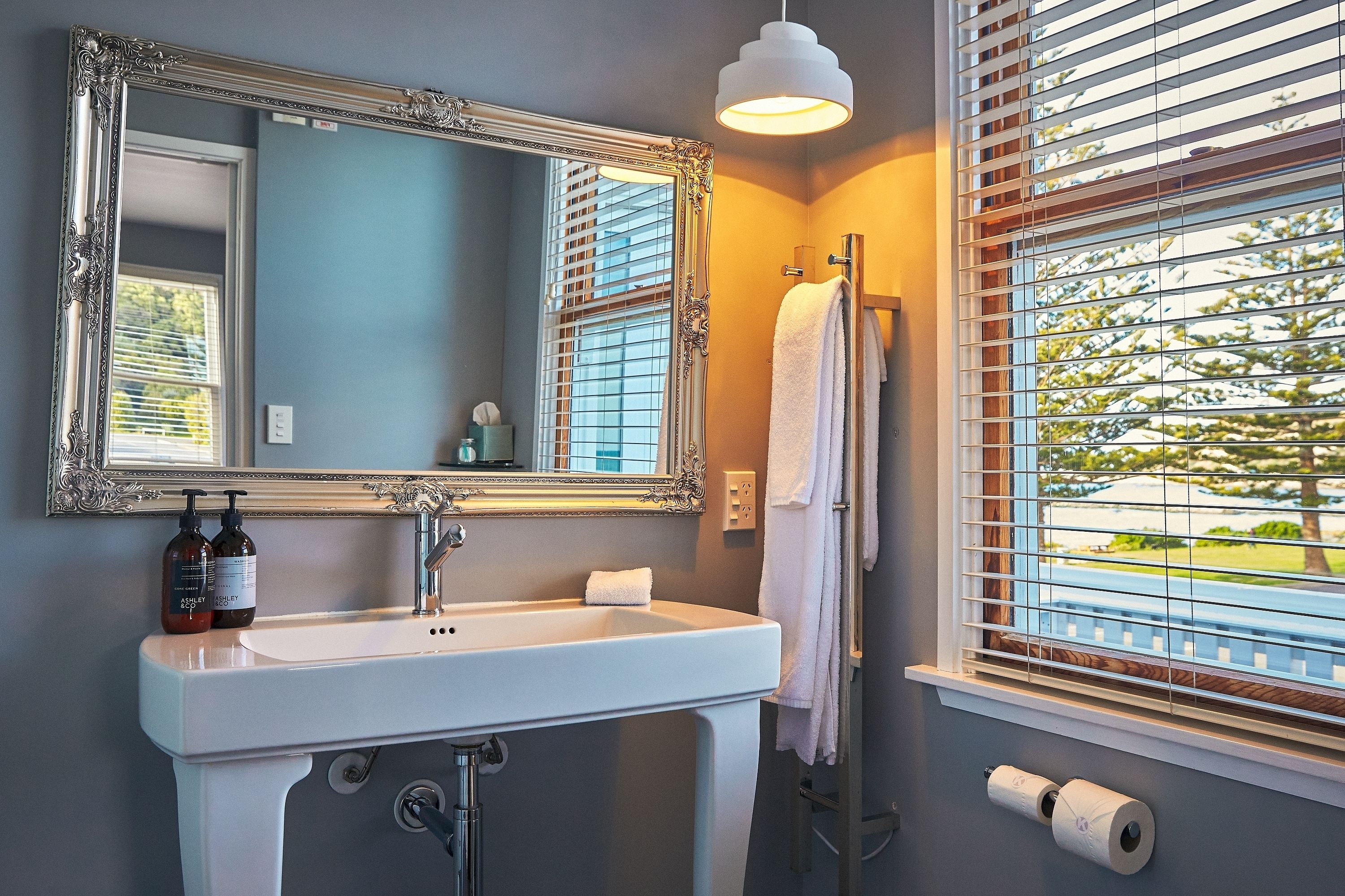 A bathroom with a white sink, a large mirror, and a window with blinds.