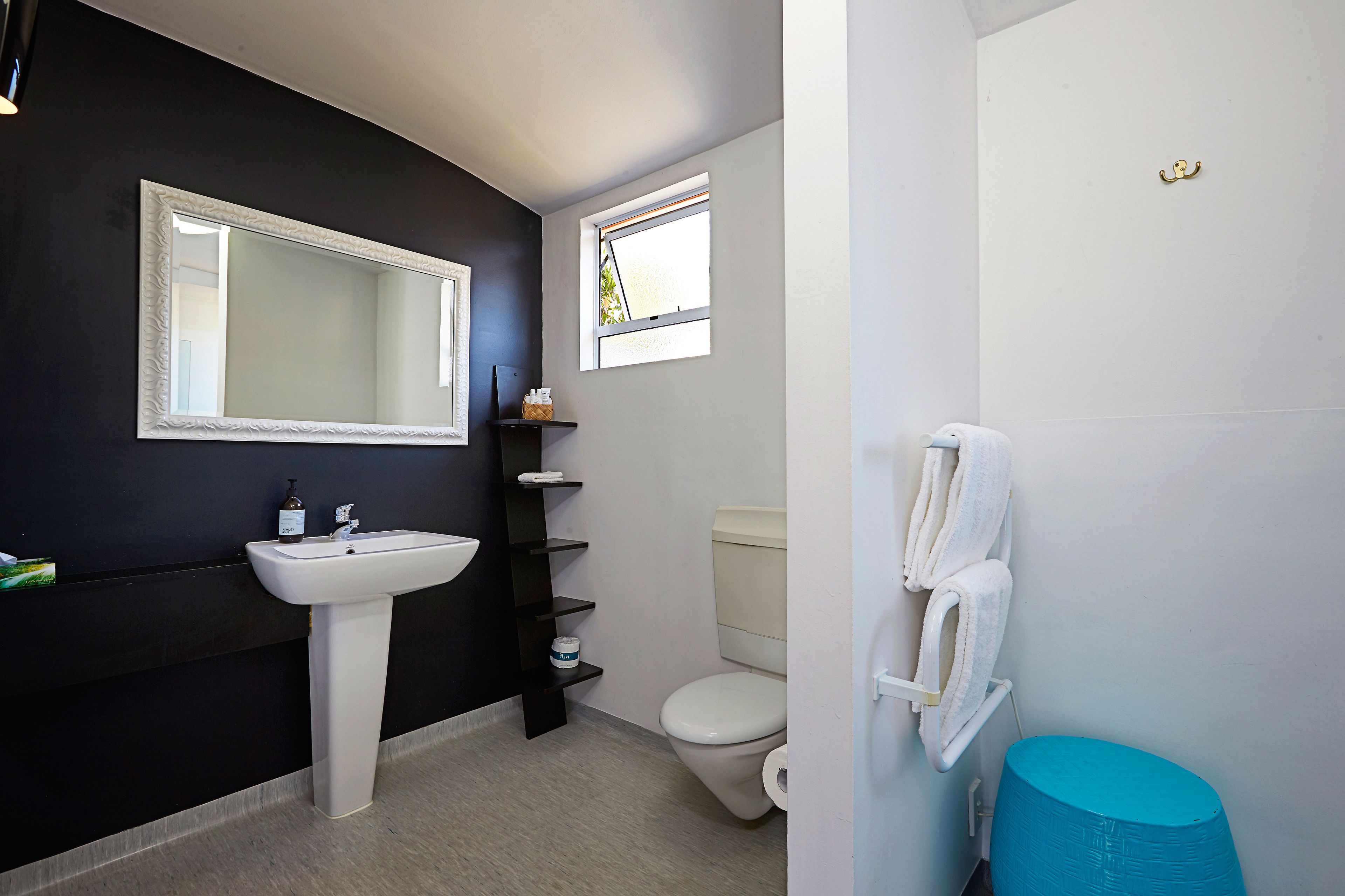 A bathroom with a white sink, a large mirror, a toilet, a blue trash bin, and a towel rack.