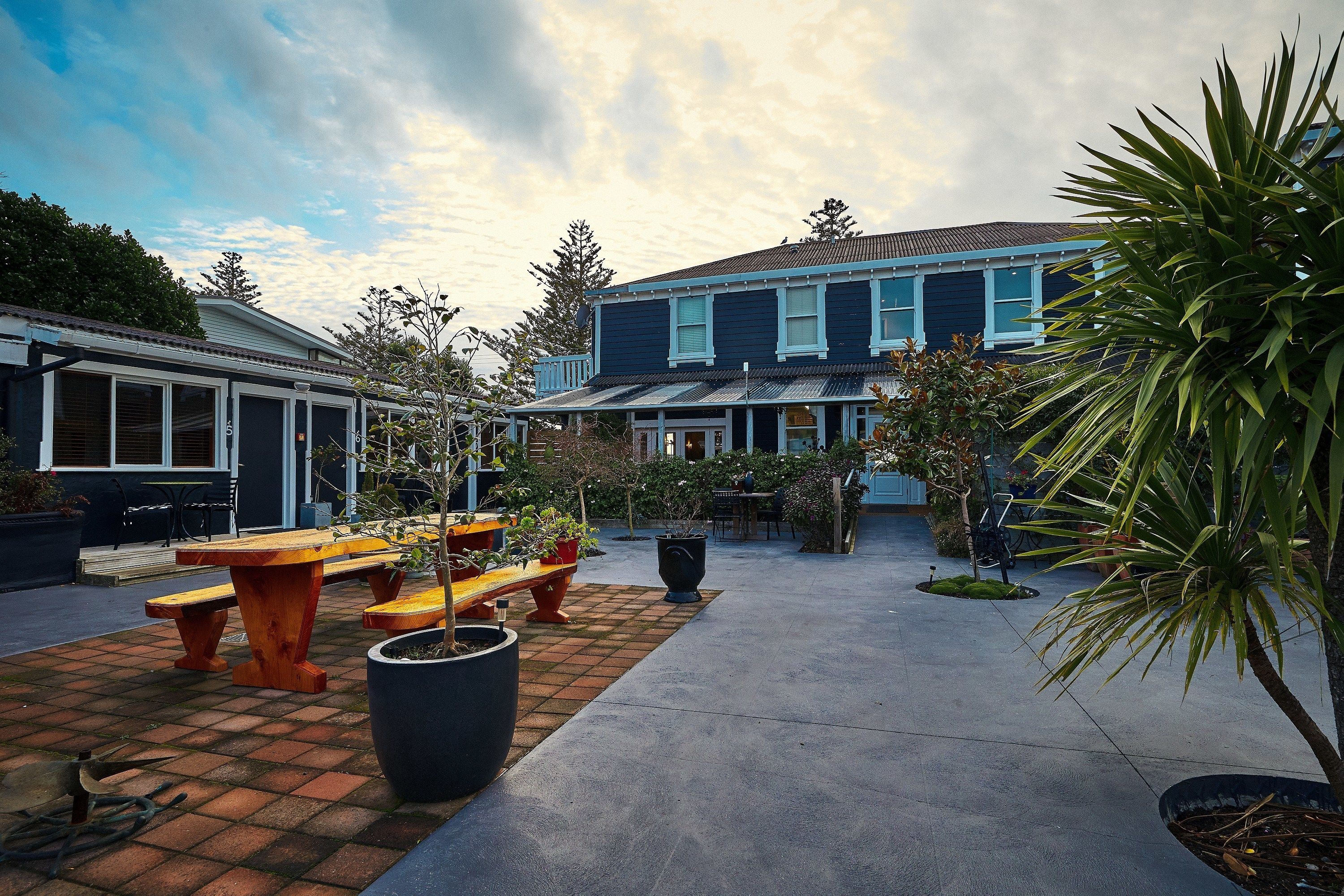 A patio with wooden benches and potted plants, a building with a blue facade, and a clear sky.