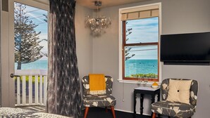 Una habitación con balcón, dos sillones, una pequeña mesa con un florero y un televisor montado en la pared.
