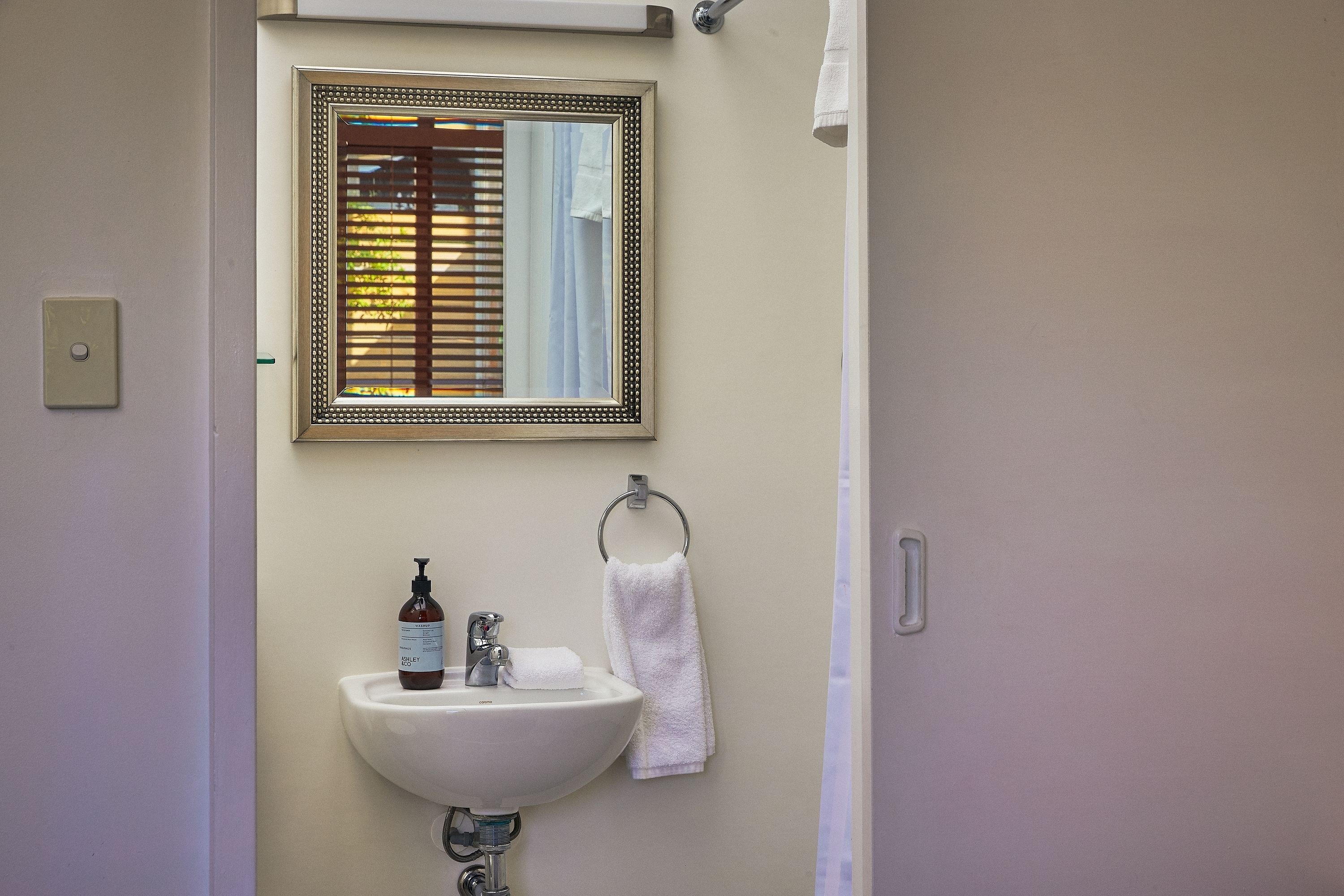 Un baño con lavamanos, espejo y perchero para toallas.