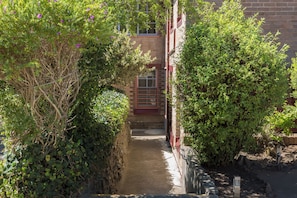 A narrow pathway flanked by dense foliage and a brick building with a window. - Katoomba Mountain Lodge (Katoomba)
