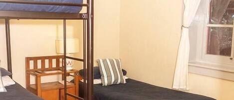 A dormitory room with bunk beds, a desk, and a chair.
