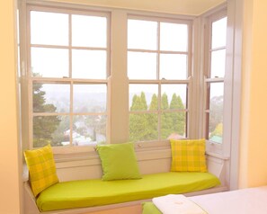 A bay window with a green cushioned bench and yellow pillows.