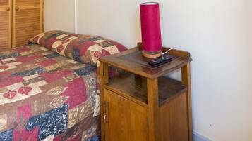 Ein Schlafzimmer mit einem hölzernen Bett, einer roten Lampe auf einem Nachttisch aus Holz und einem weißen Deckenventilator.