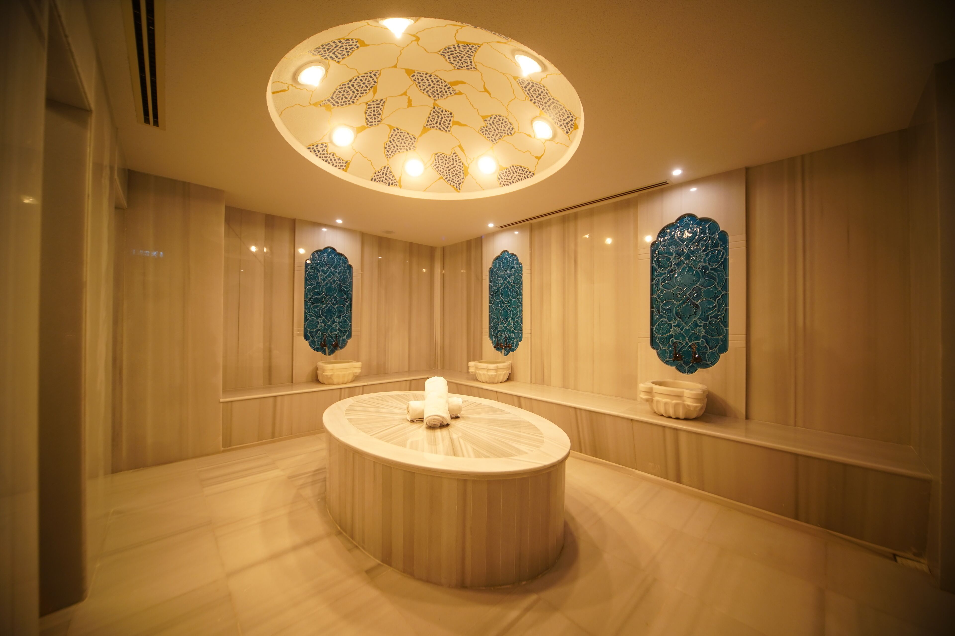 A circular seating area with a central table, surrounded by walls with decorative panels and a ceiling with a patterned light fixture.