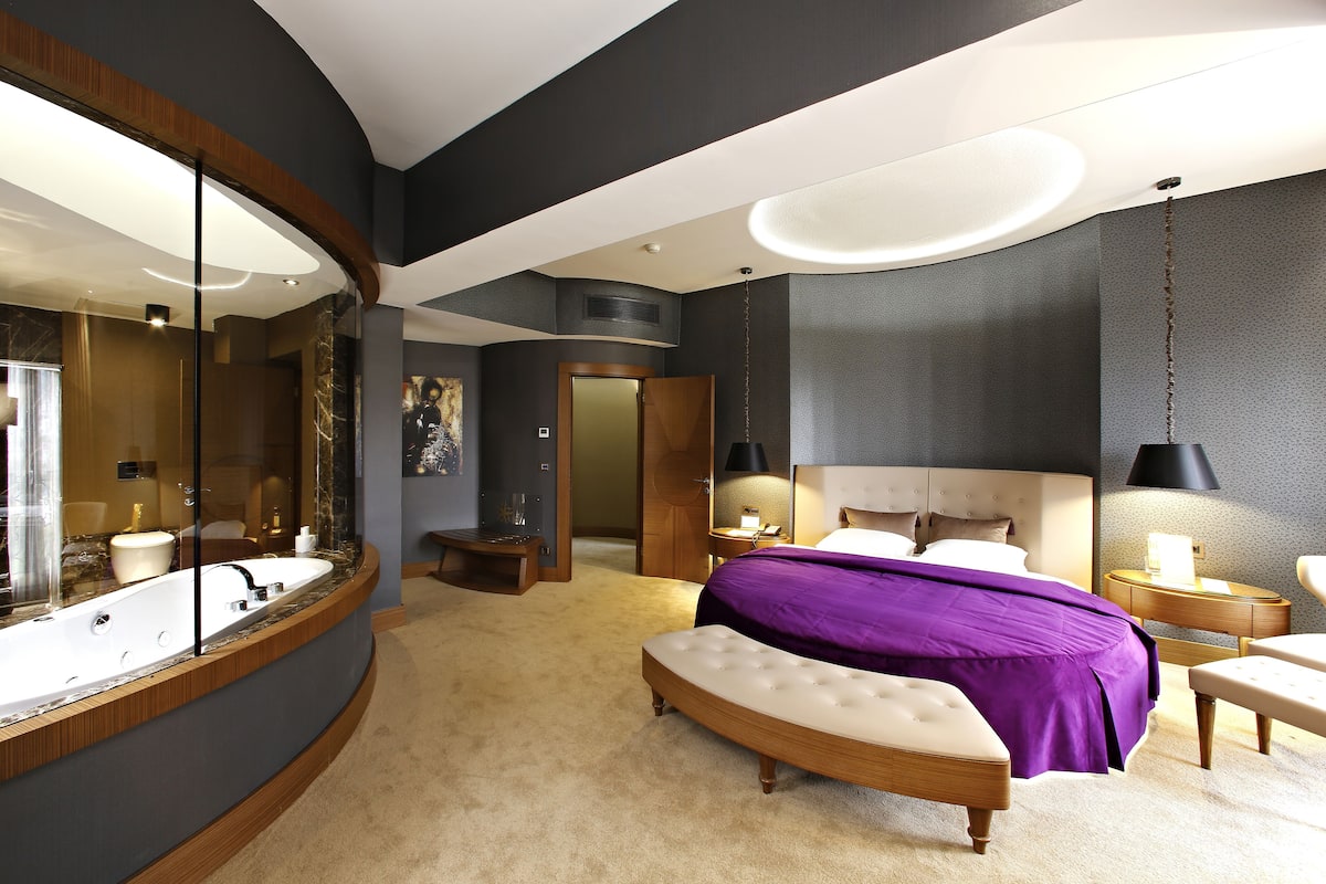 Een moderne slaapkamer met een groot bed, een gebogen kaptafel, een grote spiegel en een inloopkast.