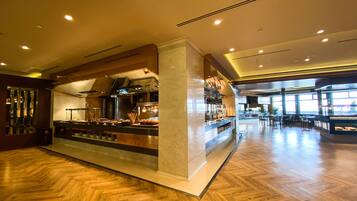 A spacious hotel lobby with a central bar area, wooden flooring, and large windows allowing natural light.