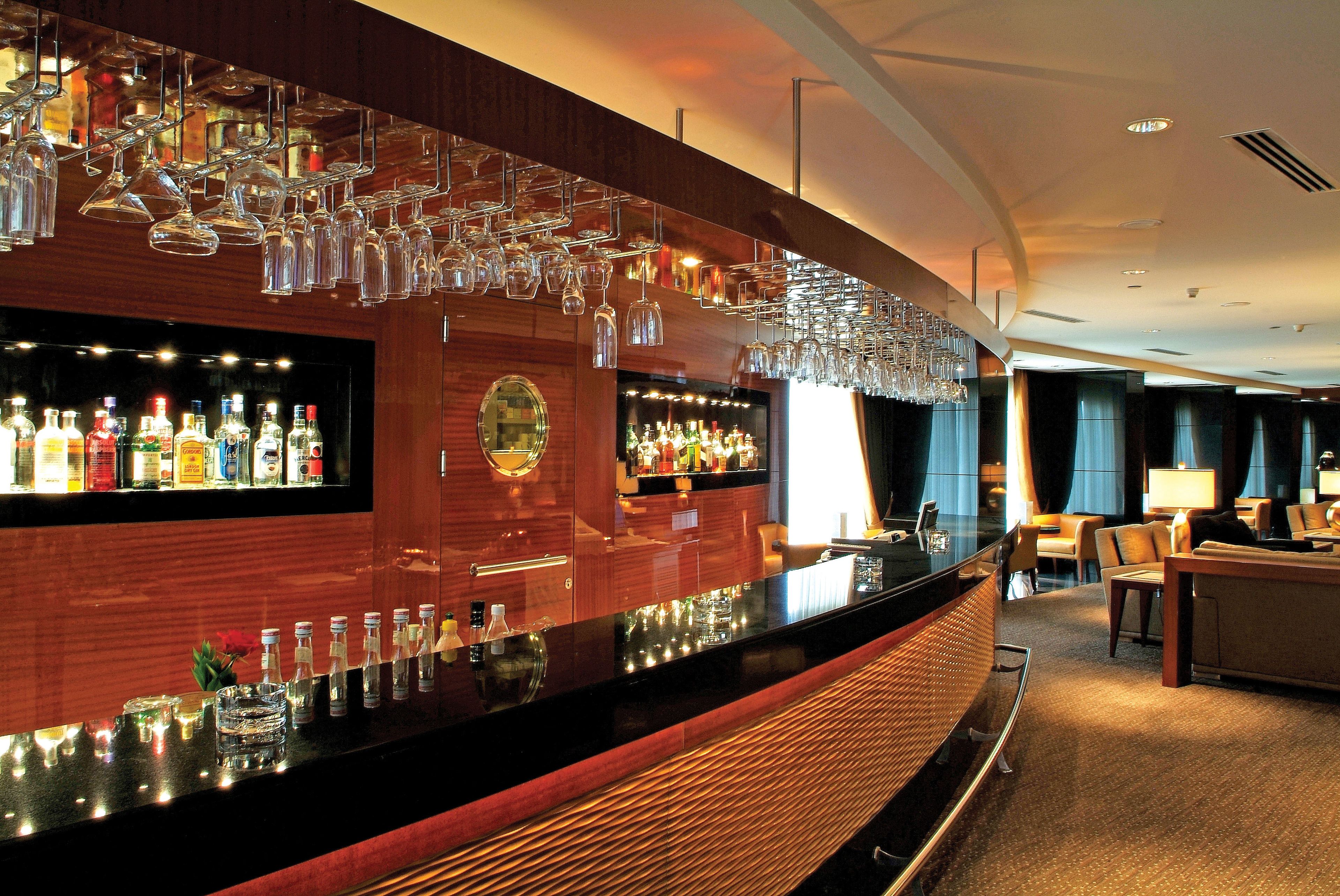 A bar area with a long counter, shelves with bottles, and hanging glasses.