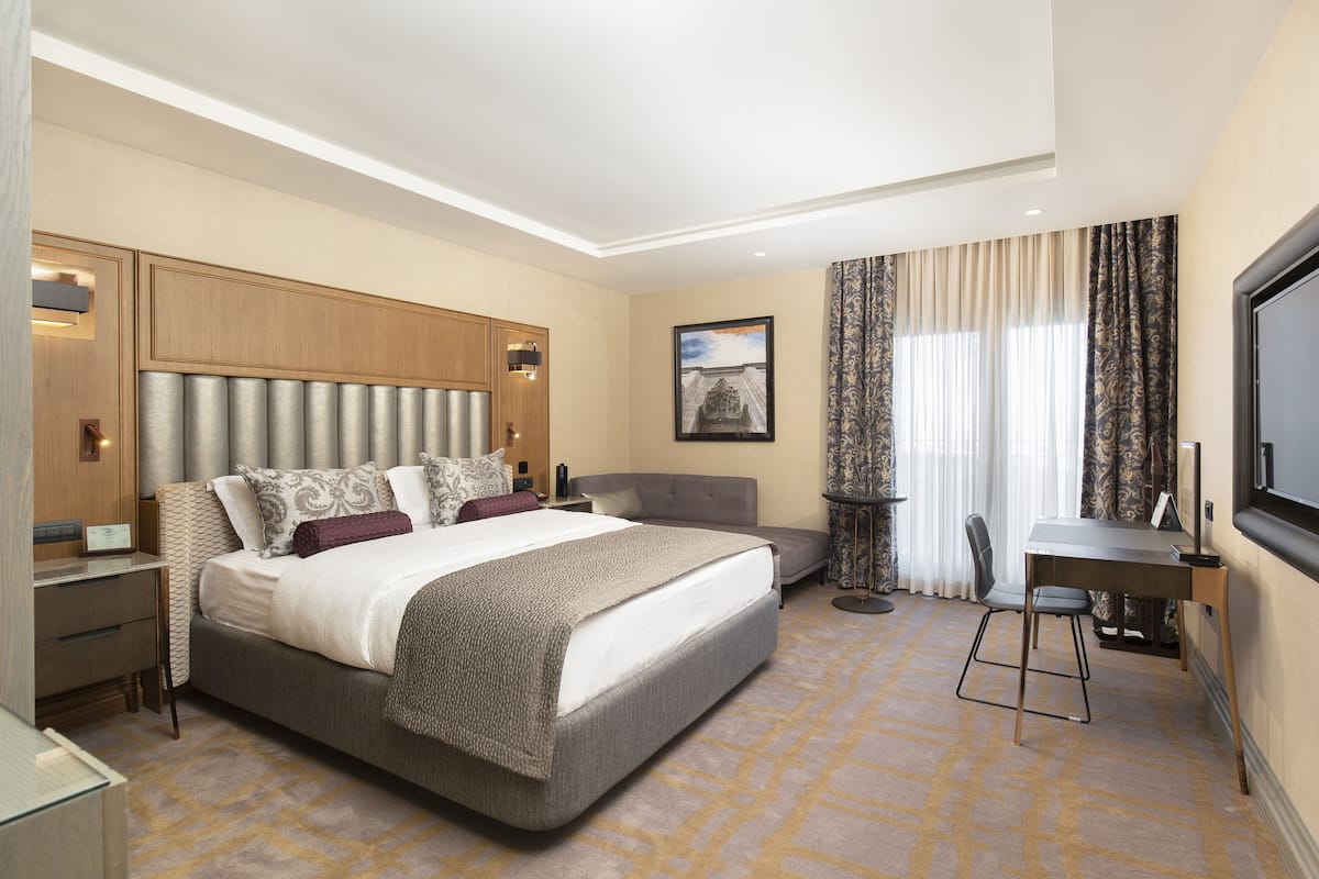 Een hotelkamer met een groot bed, een bureau en een stoel. Er is een televisie aan de muur en een raam met gordijnen.