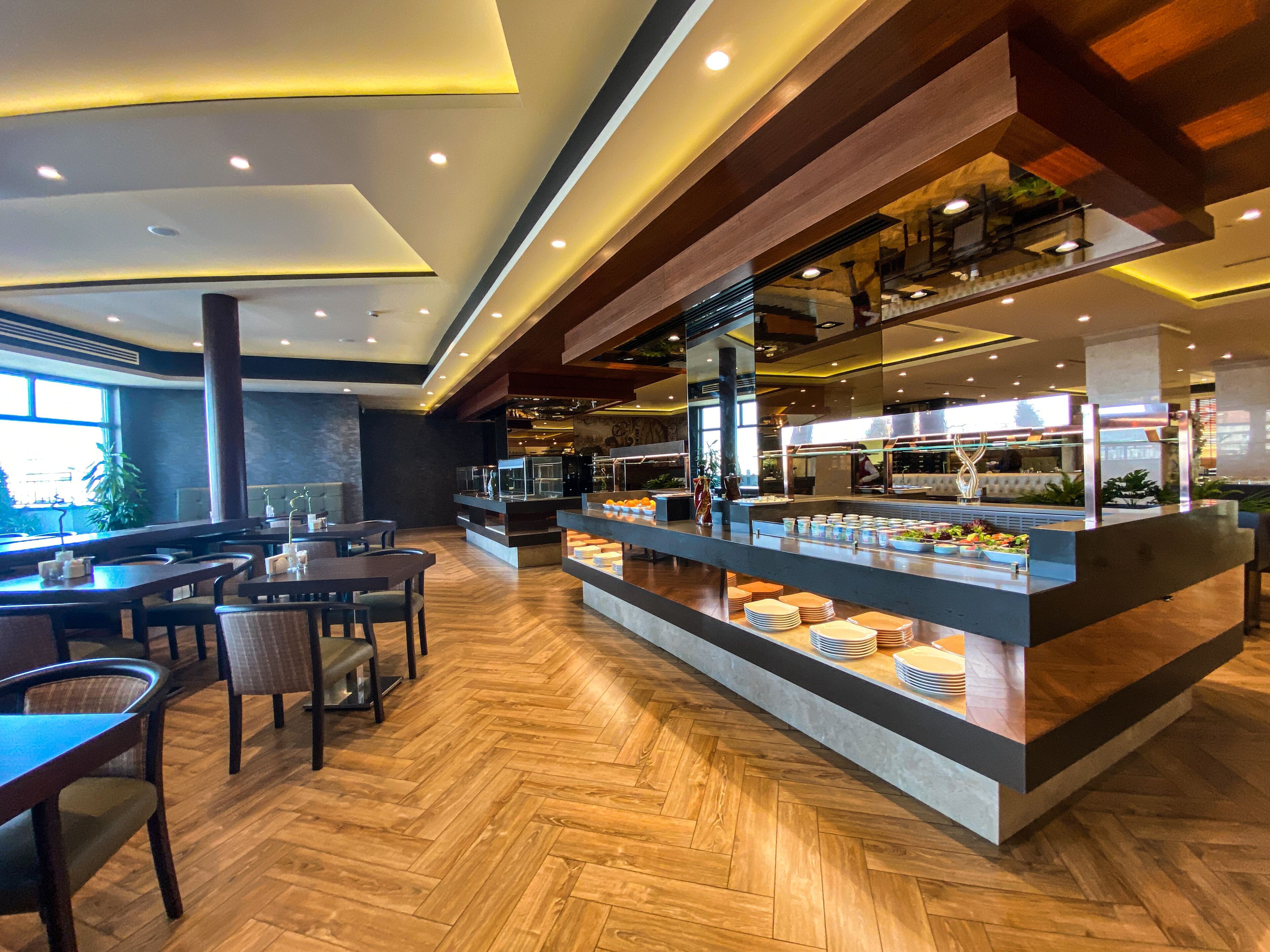 Un restaurant moderne doté d'un plancher en bois, d'un comptoir central où sont exposés les plats, et d'un espace repas avec des tables et des chaises.