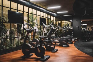 Un gimnasio con varias máquinas de ejercicio, piso de madera y ventanas amplias con plantas.