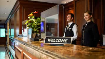 A hotel reception desk with a marble counter, a welcome sign, and a potted plant.