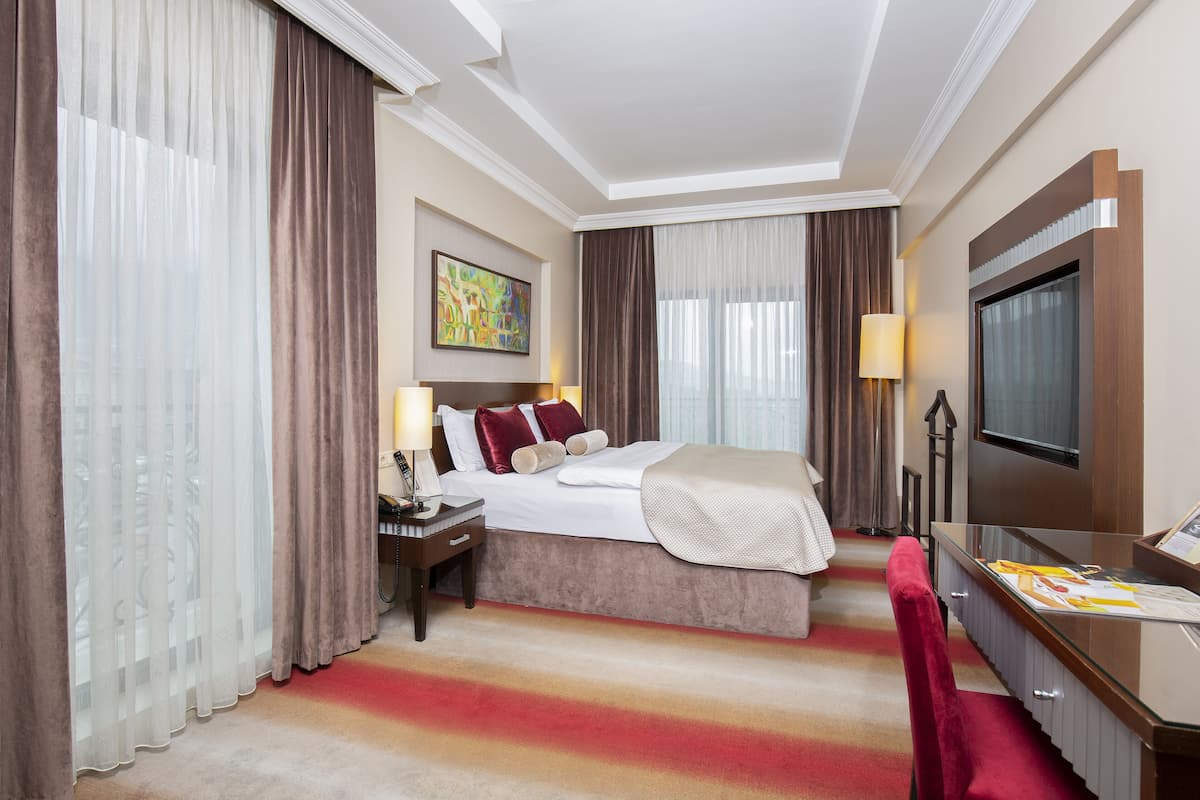 Een hotelkamer met een bed, een bureau, een televisie en gordijnen.