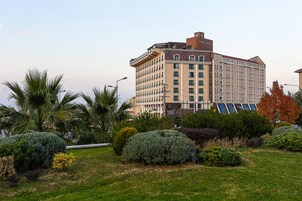 Un hotel de varios pisos con un patio central que cuenta con césped cuidado, palmeras y diversos arbustos.