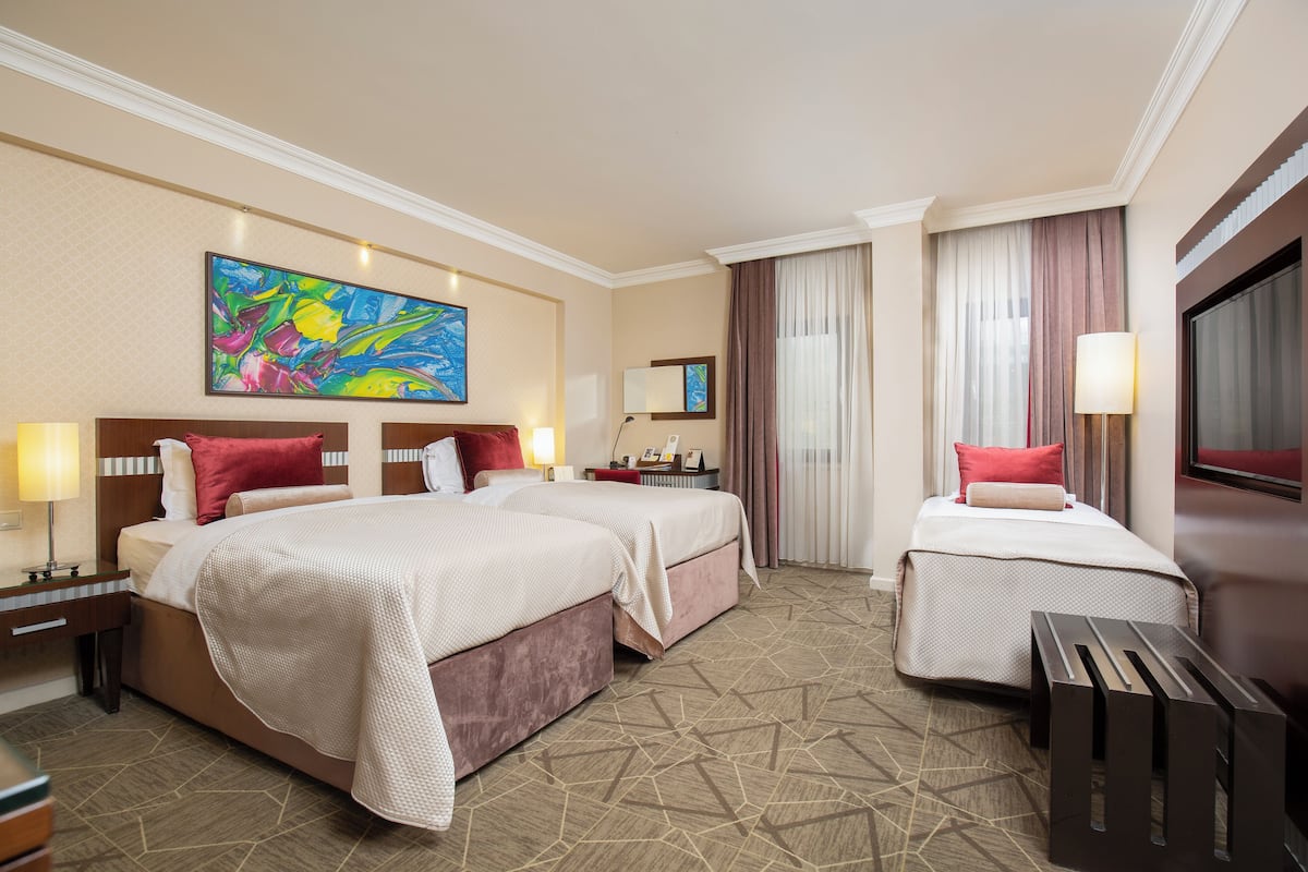 Een hotelkamer met twee bedden, een televisie, een bureau en een groot abstract schilderij aan de muur.