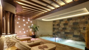 Une salle de spa avec un mur en pierre, une table de massage, un fauteuil de massage et un jacuzzi.