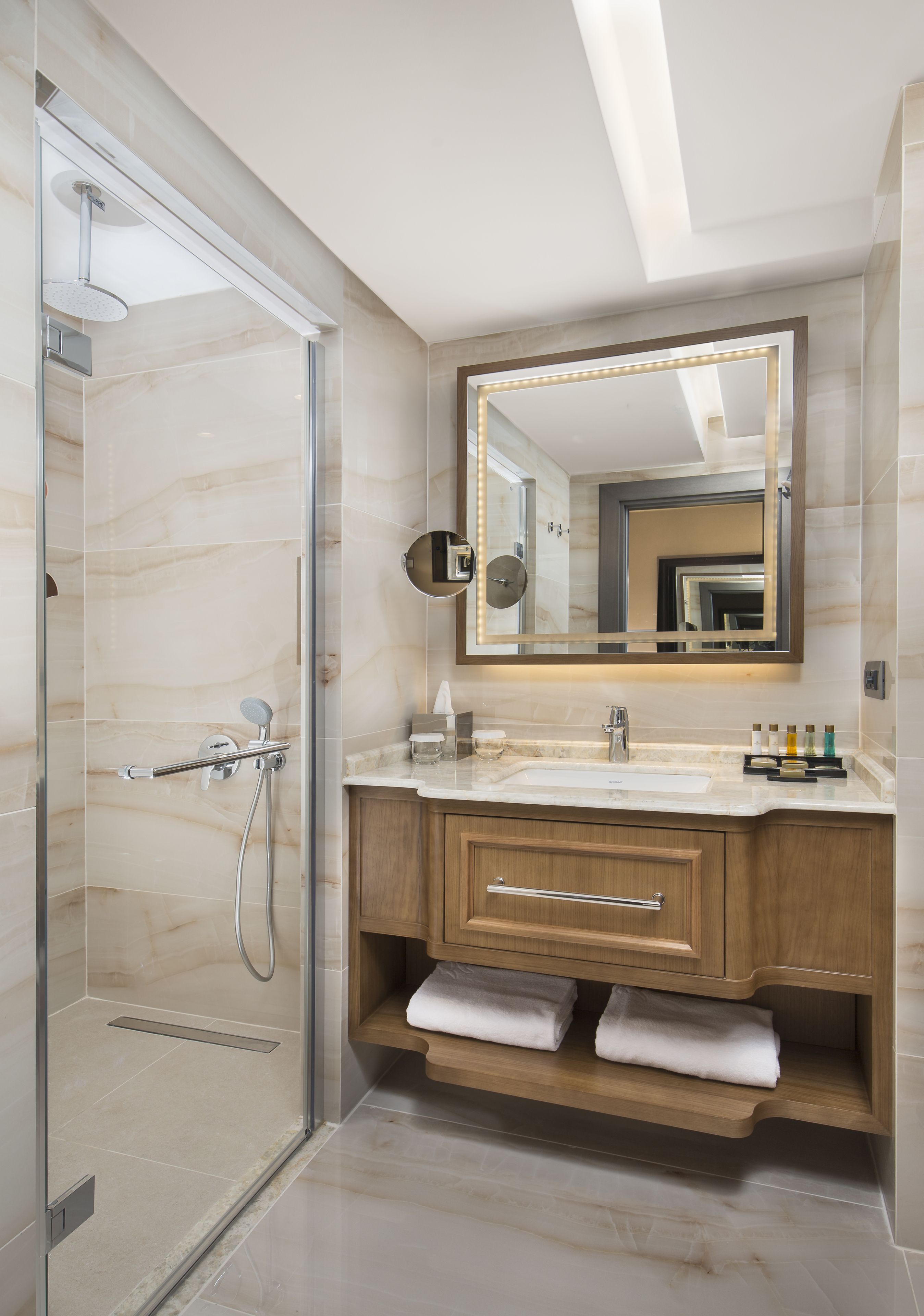 A modern bathroom with a glass shower enclosure, a vanity with a marble countertop, and a large mirror with LED lights.