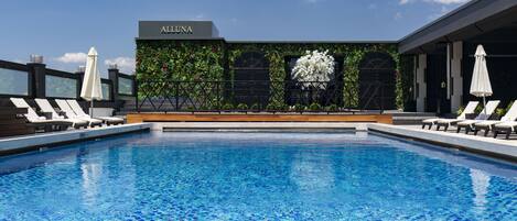 A swimming pool with a view of a building labeled "ALUNA" and a decorative wall with plants.