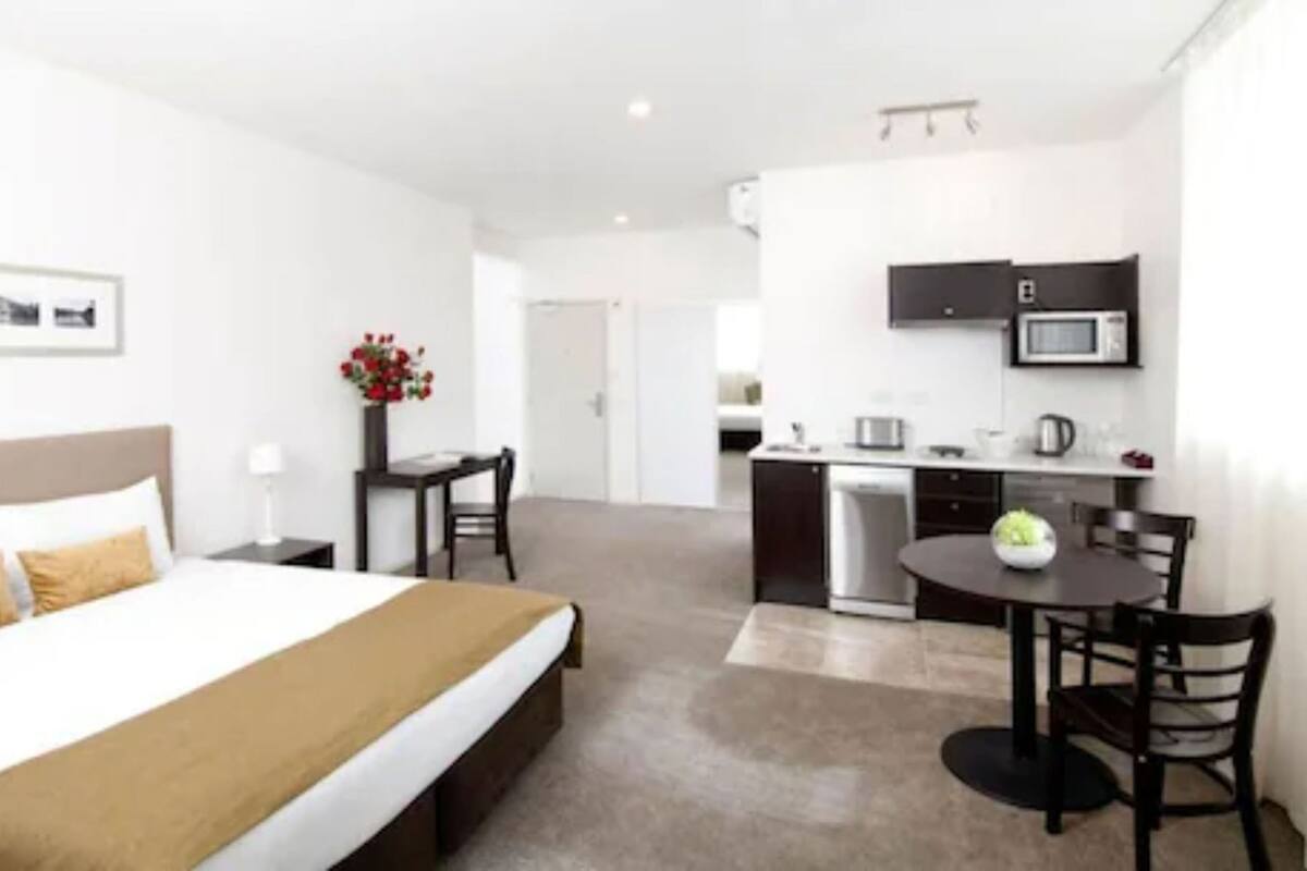 Habitación de hotel con cama, escritorio, silla, pequeña cocina y microondas.