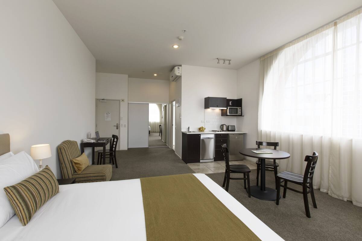 Habitación de hotel con cama, escritorio, silla, microondas y ventana con cortinas.