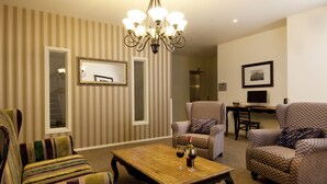 Een woonkamer met streepjesbehang, een kroonluchter, twee gestreepte fauteuils, een houten salontafel met wijnglazen en een ingelijst schilderij aan de muur.