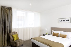 A hotel room with a bed, a chair, a nightstand, and a window with curtains.