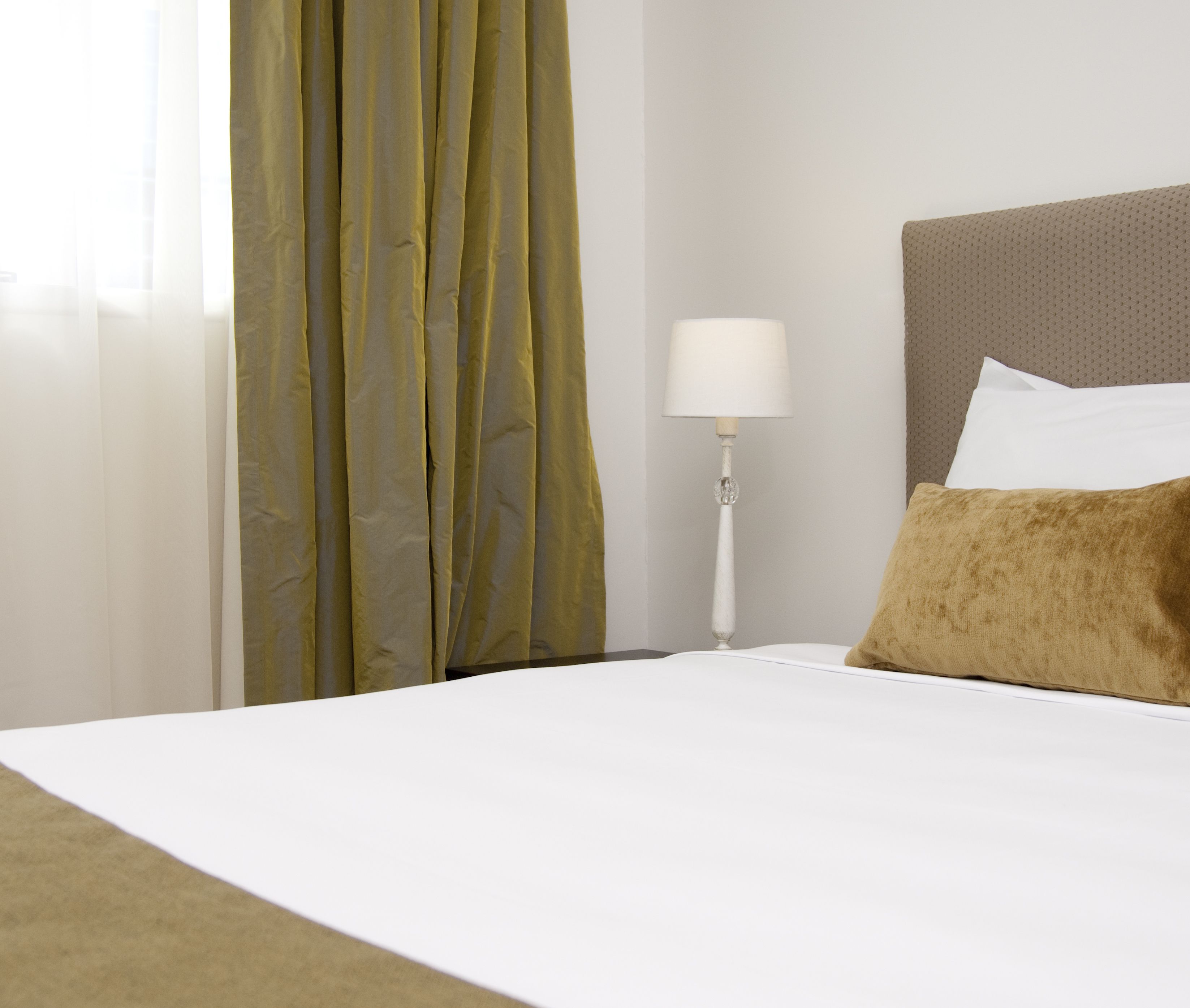 Una habitación de hotel con cama, mesita de noche con lámpara y ventana con cortinas.