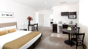 Een hotelkamer met een bed, een bureau, een stoel, een kitchenette met een magnetron en een eettafel.