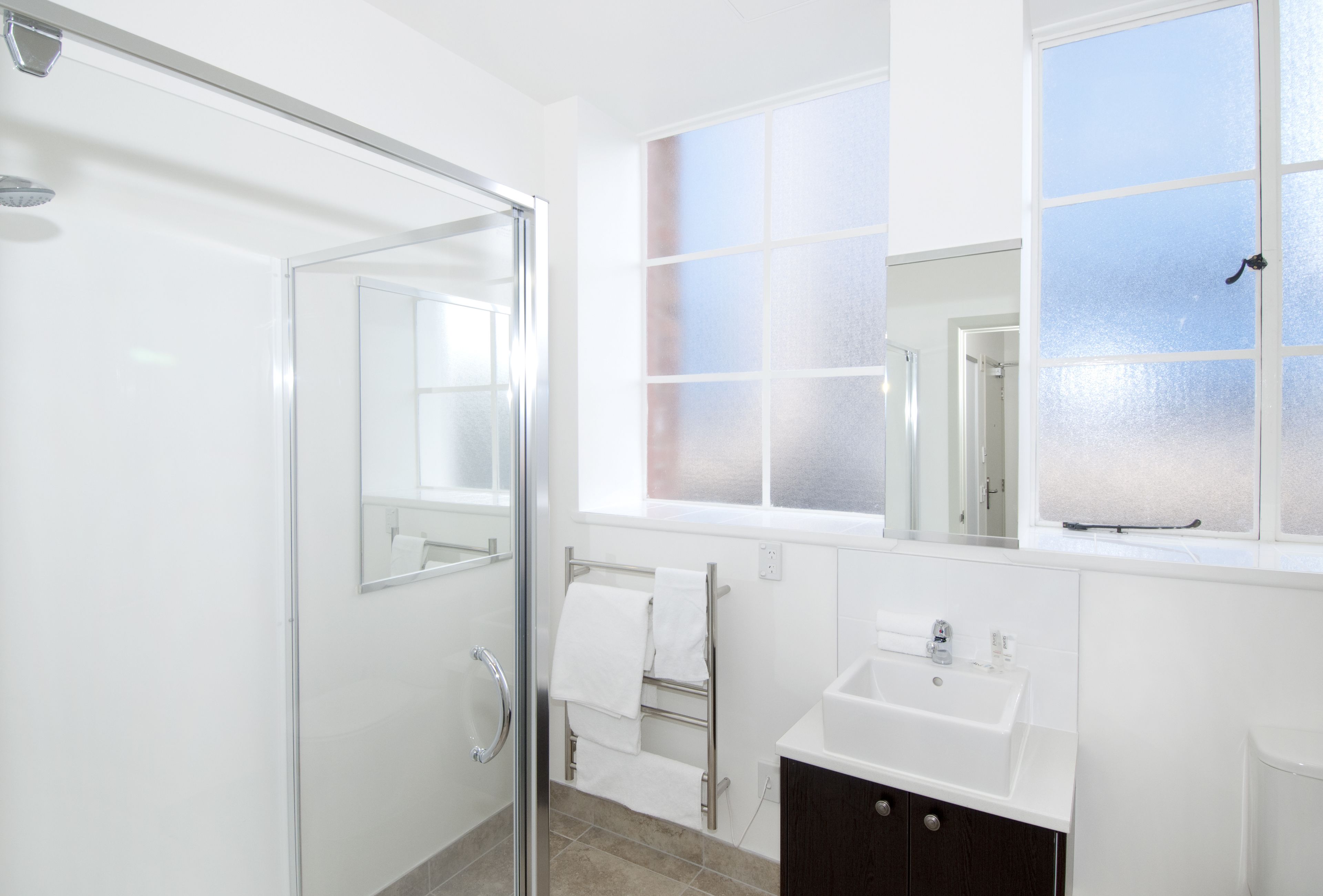 Un baño moderno con ducha de vidrio, lavamanos, toallero y ventana con vidrio esmerilado.