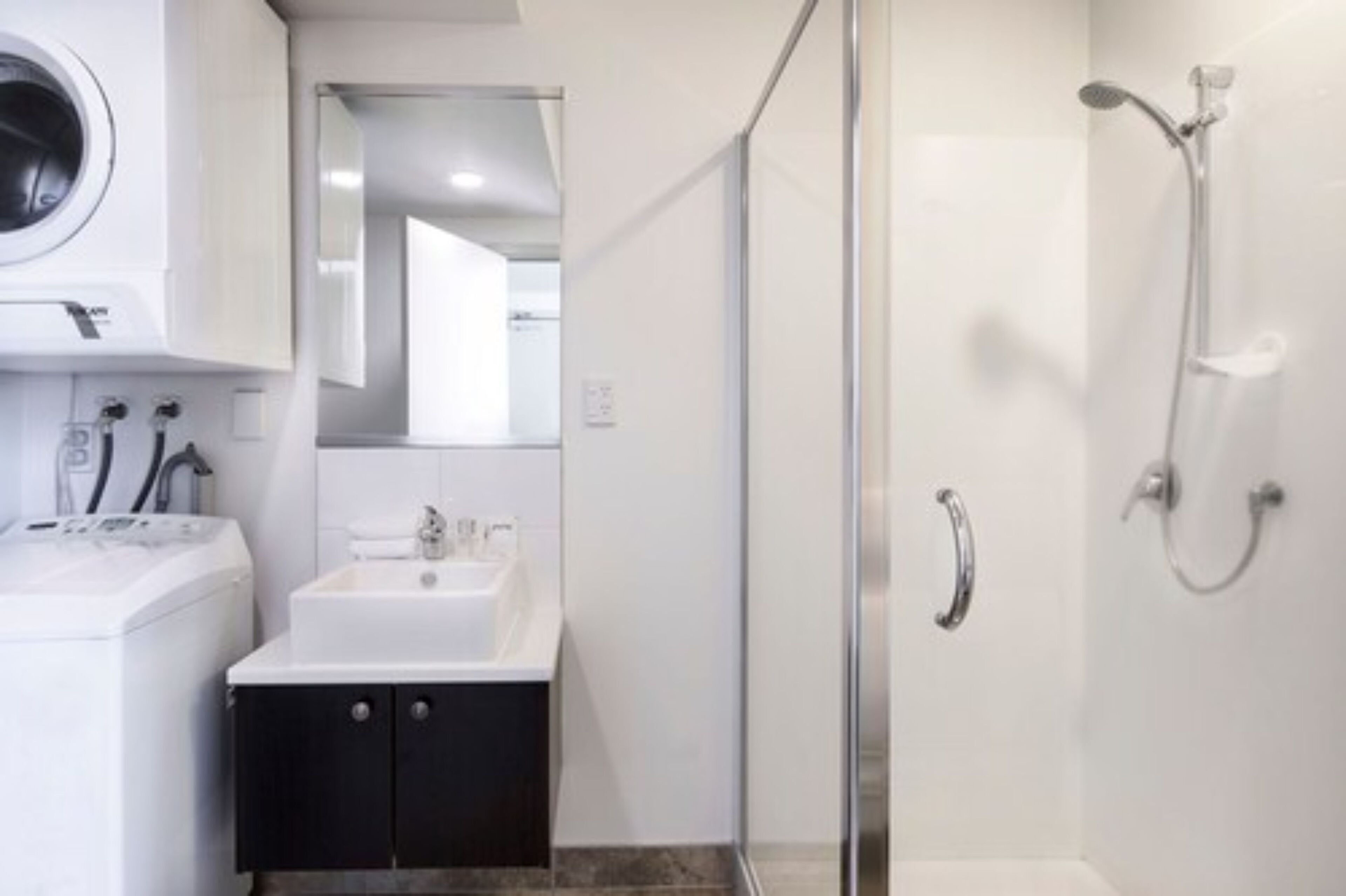 A modern bathroom with a glass-enclosed shower, a built-in washing machine, and a sink with a mirror above it.