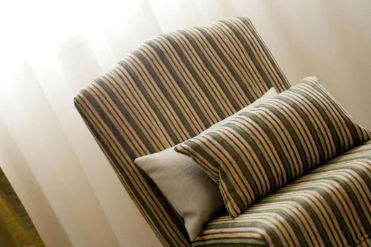 A striped armchair with a pillow, positioned against a white curtain.