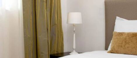 Una camera d'albergo con un letto, un comodino, una lampada e una finestra con tende.