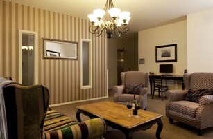 Un salón con papel tapiz a rayas, una araña de cristal, una mesa de centro de madera con copas de vino y sillones estampados.