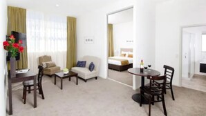 Een hotelkamer met een bank, fauteuil, eettafel en een bed met uitzicht.
