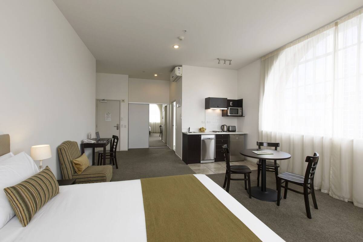 Habitación de hotel con cama, escritorio, silla, kitchenette pequeña y baño.
