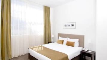 A hotel room with a bed, a nightstand, and a window with curtains.