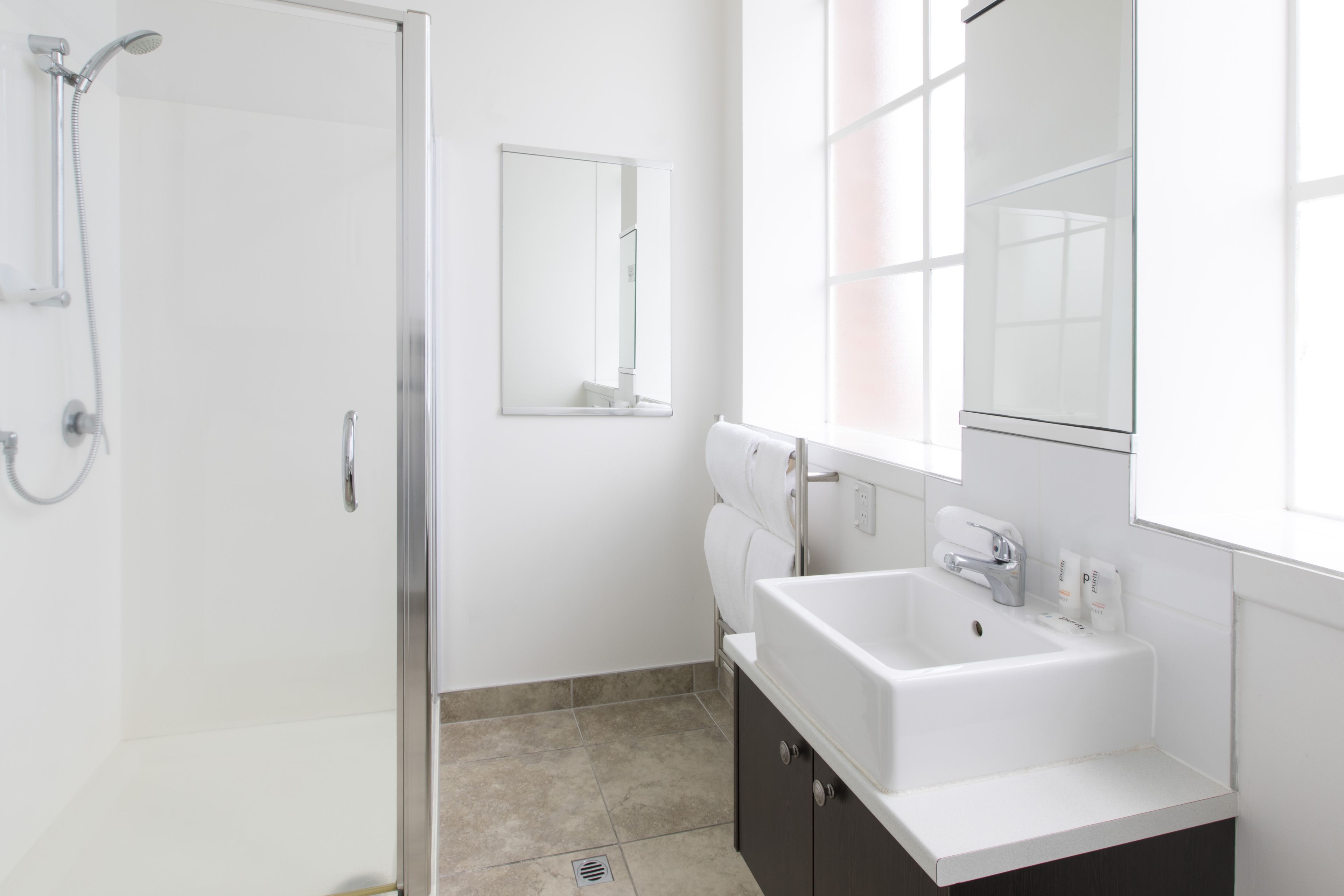 Un bagno moderno con box doccia in vetro, lavandino bianco e uno specchio grande.