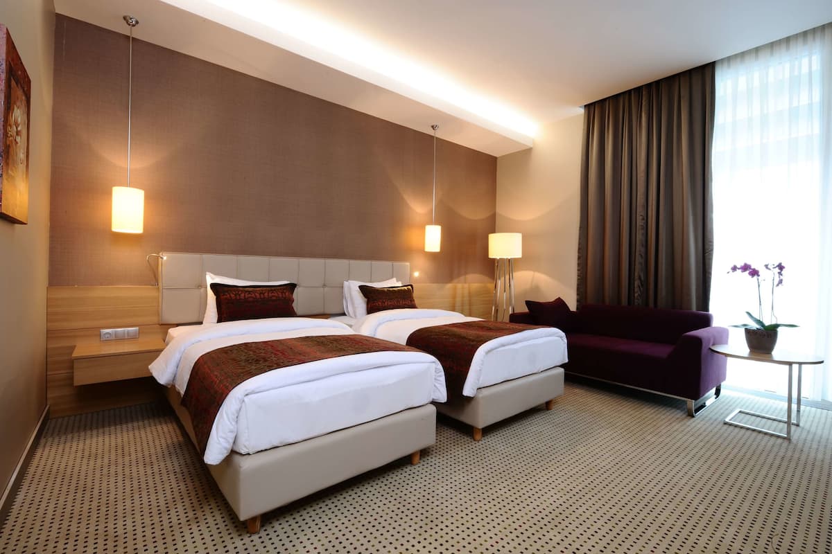 A hotel room with two beds, a sofa, a small table with a plant, and a large window with curtains.