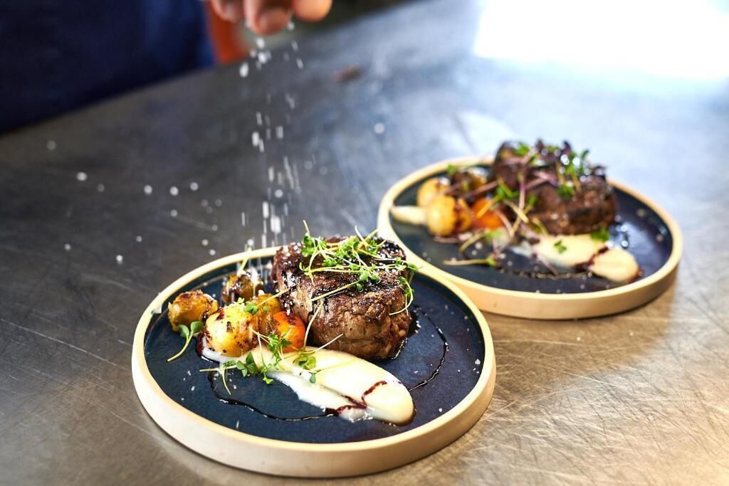 Two plates of food with a steak and vegetables on a dark plate.